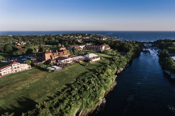Aerial view of an oceanfront hotel and event venue with a white tent and guests on the lawn near the water