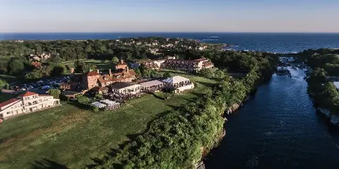 Aerial view of an oceanfront hotel and event venue with a white tent and guests on the lawn near the water