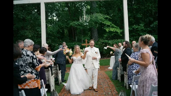 A bride and groom walking down a brick aisle after their wedding ceremony, surrounded by guests and greenery.