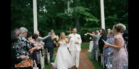 A bride and groom walking down a brick aisle after their wedding ceremony, surrounded by guests and greenery.