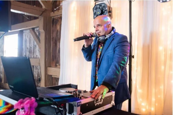 A DJ in a blue suit performing at an event with a microphone and mixing console.