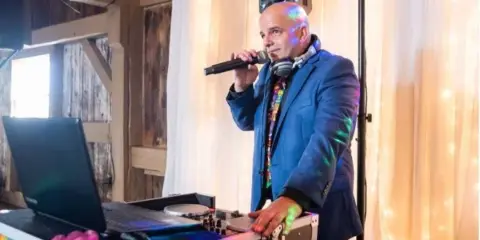 A DJ in a blue suit performing at an event with a microphone and mixing console.