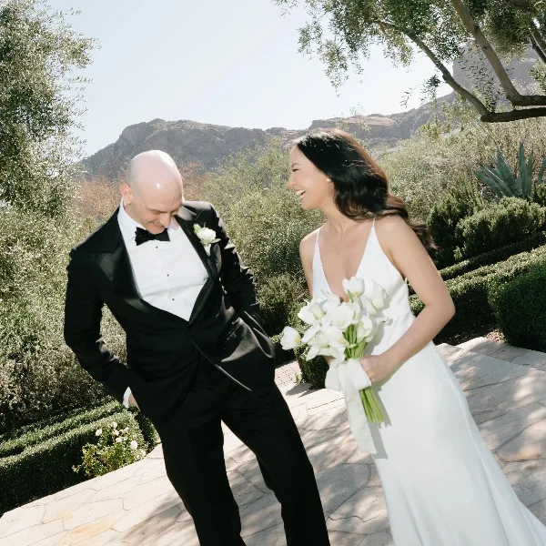 A bride holding a white bouquet and a groom wearing a boutonniere standing outdoors.