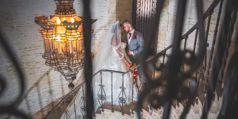 A bride and groom standing on a stone staircase with a decorative lantern in the foreground.