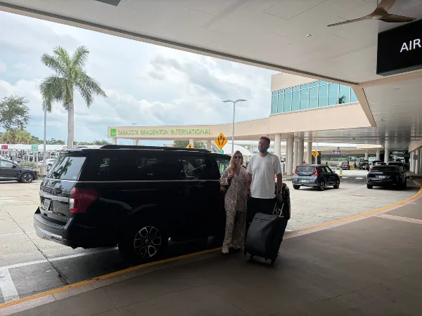 A black SUV parked at the curb of Sarasota Bradenton International Airport with a passenger and luggage.