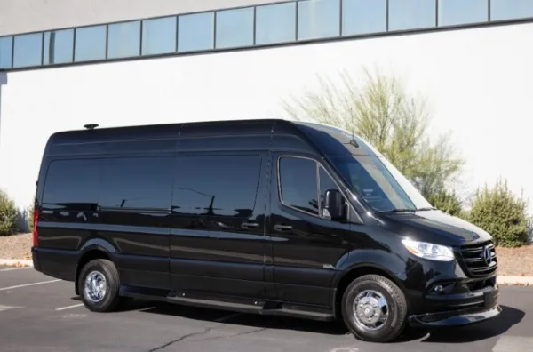 A black passenger van parked in a lot in front of a modern building.