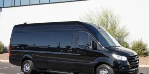 A black passenger van parked in a lot in front of a modern building.