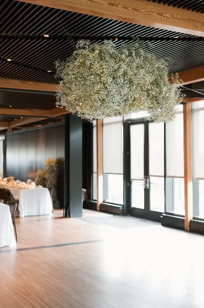 A large, cloud-like floral arrangement of white gypsophila suspended from the ceiling of a modern event venue.