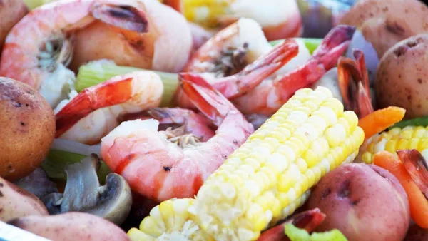 Close-up of a catering platter with cooked shrimp, corn on the cob, potatoes, and vegetables.