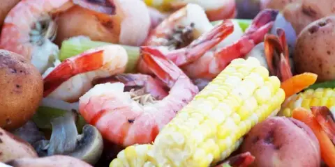 Close-up of a catering platter with cooked shrimp, corn on the cob, potatoes, and vegetables.