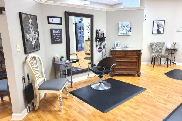 Interior view of a hair salon with a styling chair, mirror, and wooden flooring.