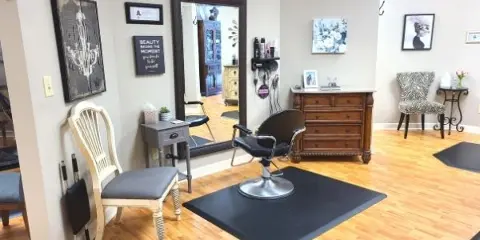 Interior view of a hair salon with a styling chair, mirror, and wooden flooring.