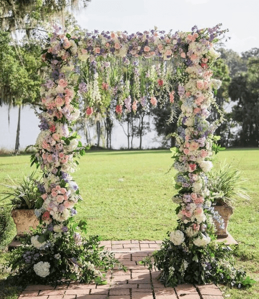 A floral wedding arch decorated with pastel flowers and greenery in a sunny garden.