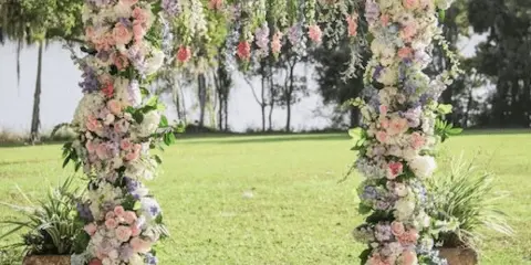 A floral wedding arch decorated with pastel flowers and greenery in a sunny garden.