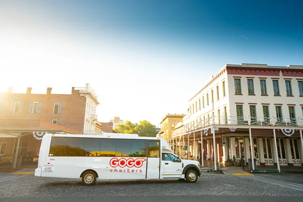 A white GOGO Charters shuttle bus parked on a cobblestone street in front of historic buildings.