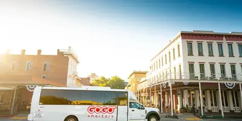 A white GOGO Charters shuttle bus parked on a cobblestone street in front of historic buildings.