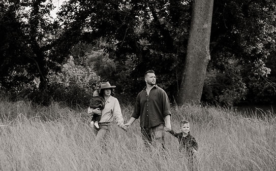 Black and white photograph of a couple holding hands with their two young children in a grassy field.