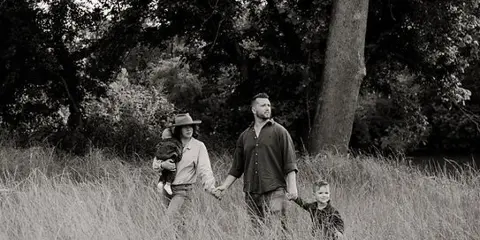 Black and white photograph of a couple holding hands with their two young children in a grassy field.