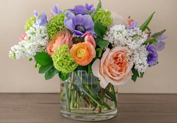 A colorful floral arrangement featuring roses, anemones, and hydrangeas in a clear glass vase.