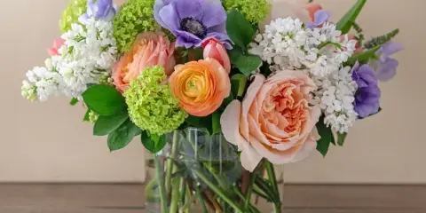 A colorful floral arrangement featuring roses, anemones, and hydrangeas in a clear glass vase.