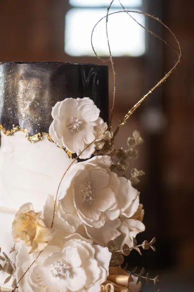 A close-up of a white and black wedding cake decorated with white sugar flowers and gold accents.