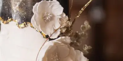 A close-up of a white and black wedding cake decorated with white sugar flowers and gold accents.