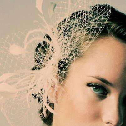 Close-up of a woman's face with an elegant updo hairstyle and a white decorative fascinator.