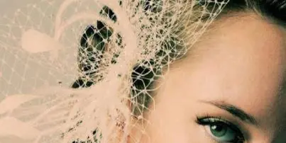 Close-up of a woman's face with an elegant updo hairstyle and a white decorative fascinator.