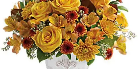 A vibrant floral arrangement featuring yellow roses, alstroemeria, and dahlias in a white ceramic vase.