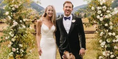 A bride and groom posing with a dog in front of floral wedding arches with a mountain background.