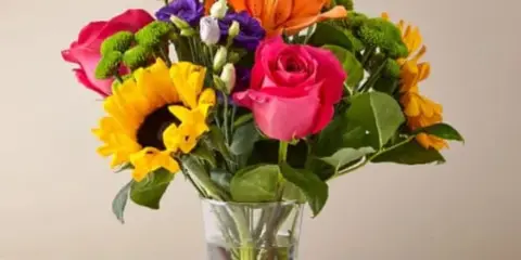Mixed bouquet of roses, lilies, sunflowers, and purple blooms in a glass vase