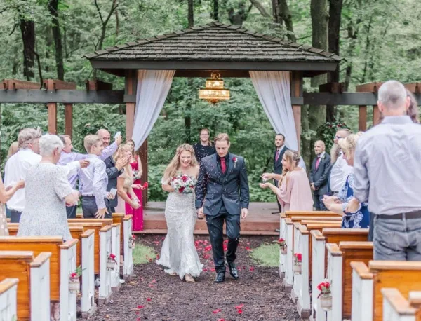 A bride and groom walking down the aisle at an outdoor wedding ceremony under a wooden pergola.