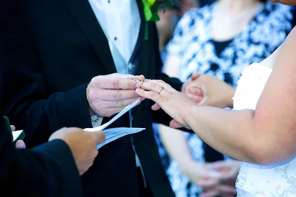A close-up of a wedding officiant placing a ring on a bride's finger during a ceremony.