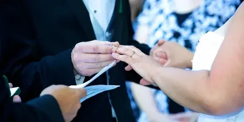 A close-up of a wedding officiant placing a ring on a bride's finger during a ceremony.