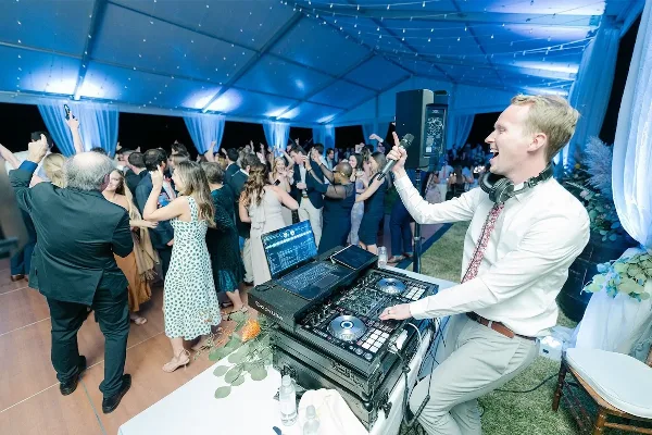 A professional DJ performing at a wedding reception with a packed dance floor.