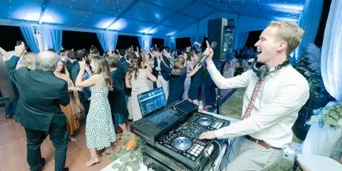 A professional DJ performing at a wedding reception with a packed dance floor.