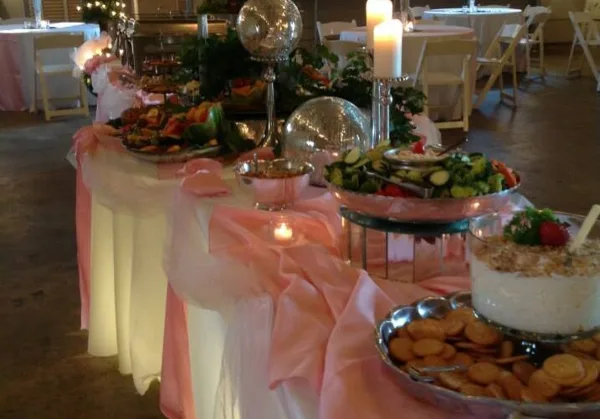 Decorated catering buffet table with food platters, candles, and pink table runners at a wedding event