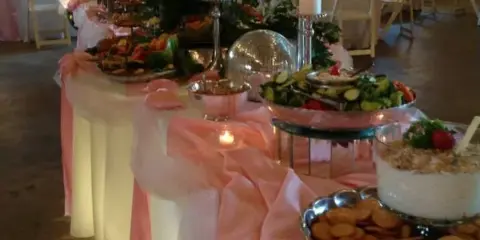 Decorated catering buffet table with food platters, candles, and pink table runners at a wedding event