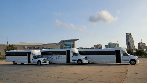 Three white party buses parked in a row in a paved lot during the day.