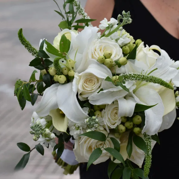 White rose and calla lily bouquet with green berries and foliage held by a person