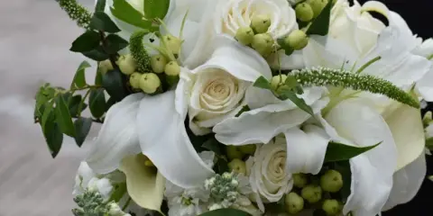 White rose and calla lily bouquet with green berries and foliage held by a person
