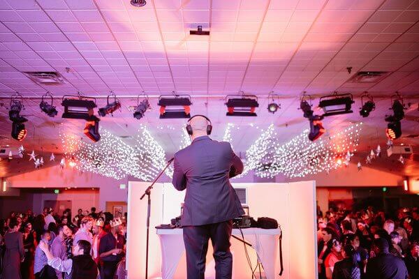 A DJ performing at a crowded event venue with stage lighting and a large audience.