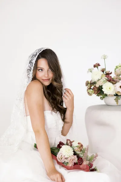 A bride in a white dress and veil posing with a bouquet of flowers.