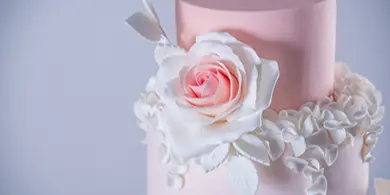 A close-up of a pink two-tier wedding cake decorated with a large white and pink sugar rose and delicate sugar leaves.
