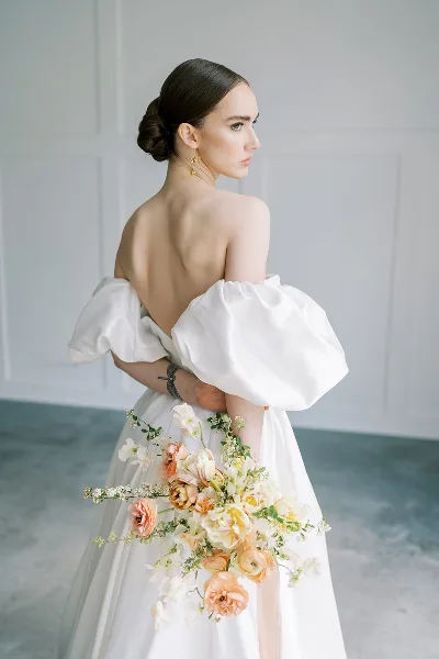 Bride in profile wearing an elegant updo and white gown, holding a bouquet.