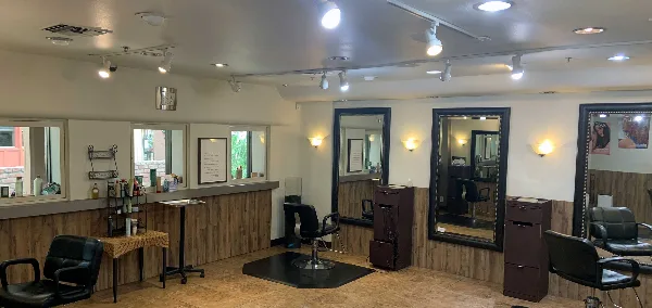Interior of a hair salon with black styling chairs, large mirrors, track lighting, and product displays.