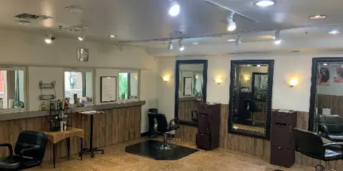 Interior of a hair salon with black styling chairs, large mirrors, track lighting, and product displays.
