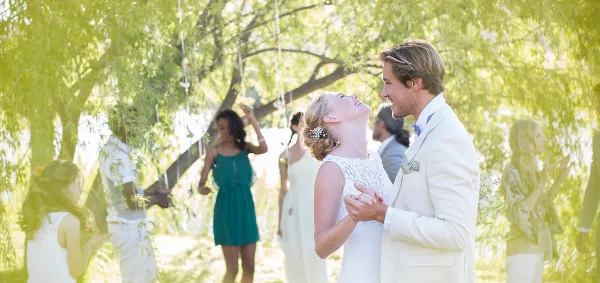 A bride and groom dancing at an outdoor wedding reception with guests in the background.