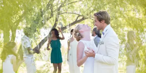 A bride and groom dancing at an outdoor wedding reception with guests in the background.