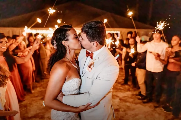 A bride and groom sharing a kiss during a sparkler send-off under a large tent at a rustic wedding venue.